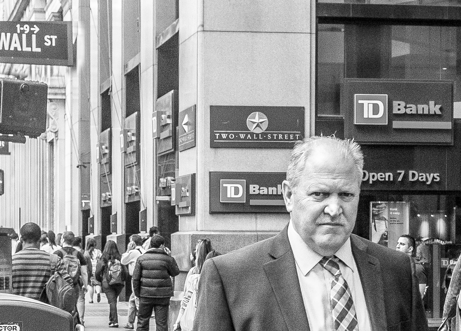 Man in a suit walking; surrounding crowd passing by, TD Bank building with “Two Wall Street” and “Open 7 Days” signage visible.