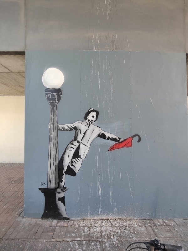 a painting of a man twirling around a light pole in a rainstorm holding a red umbrella