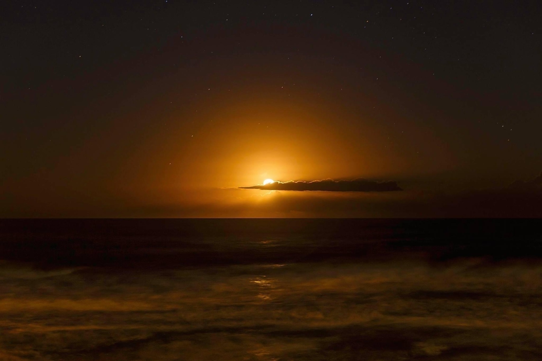 A glowing moon over the ocean creates a warm, orange hue in the sky, with a cloud partially obscuring the light.