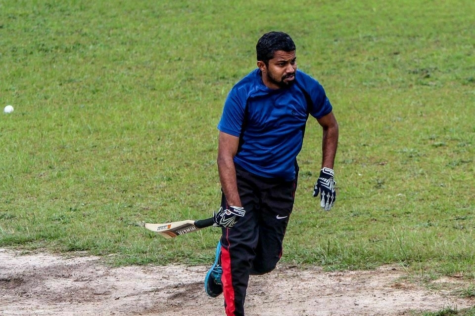 A man wearing a blue shirt and black pants is playing cricket on a grassy field.