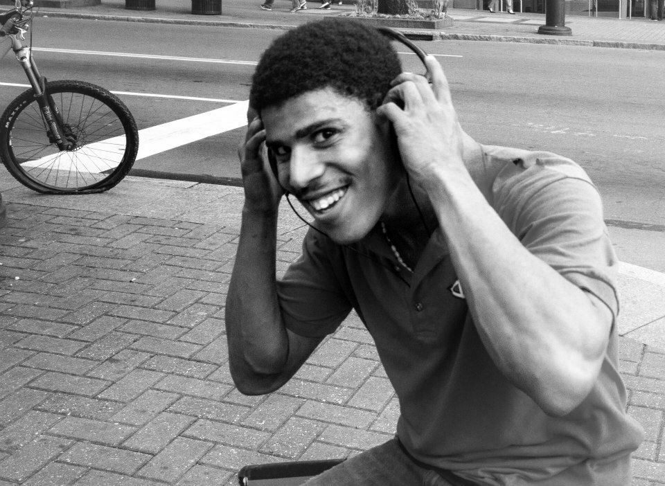 A young man taking off his headphones to engage in conversation on the sidewalk