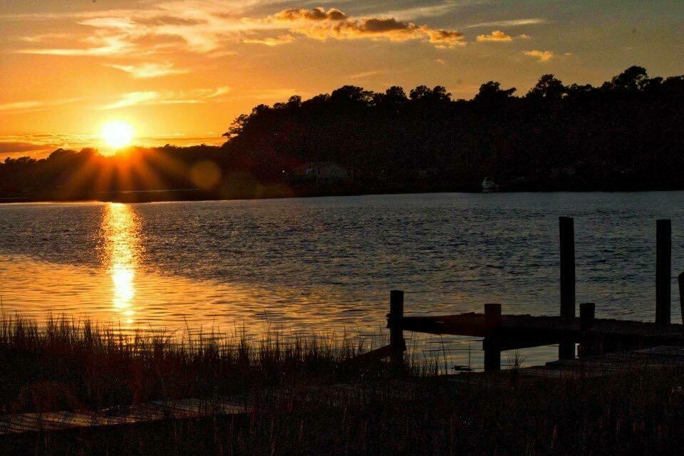 A serene sunset over a calm lake with silhouetted trees and a dock in the foreground.