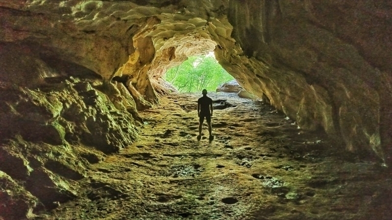 A photo taken inside a cave with a man standing between the camera and the cave entrance