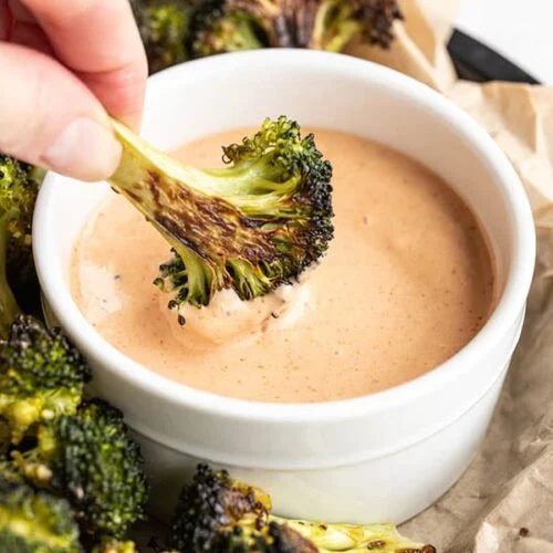 Broccoli dipped into a reddish pink sauce in a white bowl