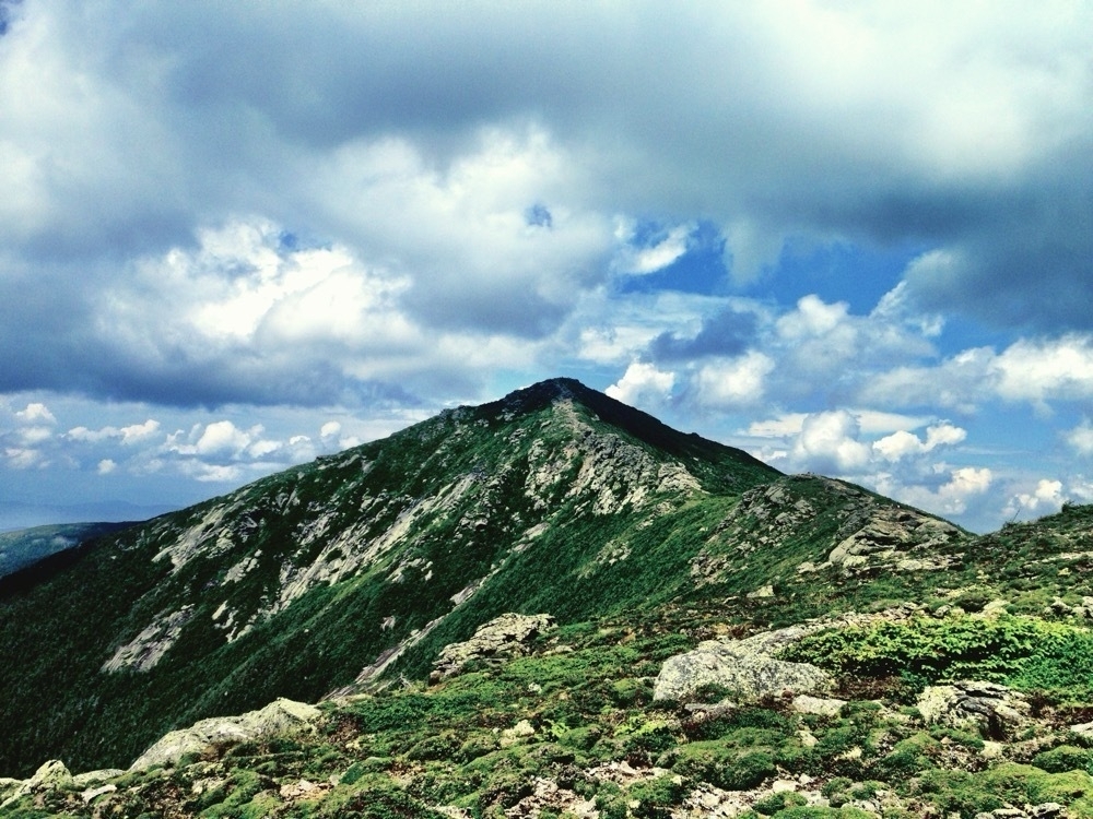 The green and granite summit of Lincoln as seen from the footpath of the Appalachian Trail atop Franconia Ridge in the White Mountains of New Hampshire.