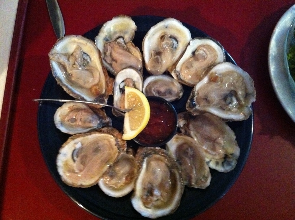 A plate of raw oysters served with a lemon wedge and cocktail sauce.