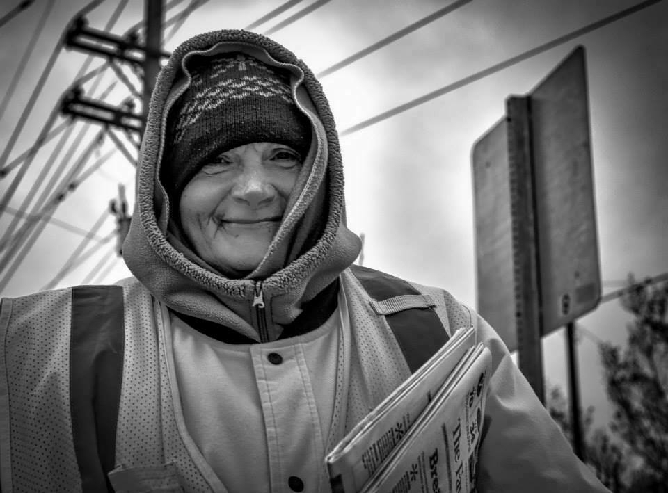 A smiling newspaper vendor in cold weather head gear