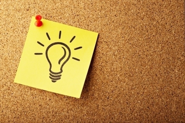 A yellow sticky note with a lightbulb drawing thumb-tacked to a corkboard