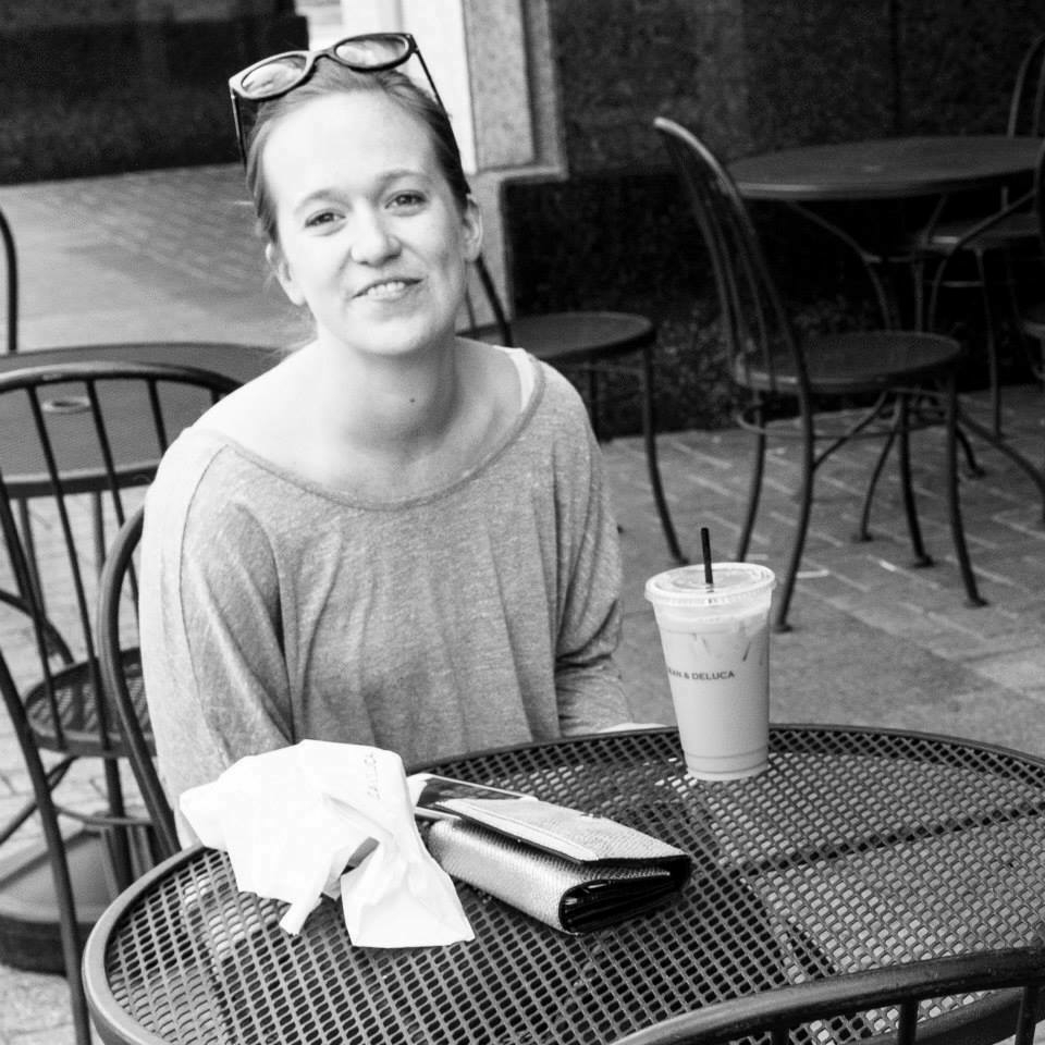 A smiling woman at an outdoor cafe, seated at a table with a cup of coffee