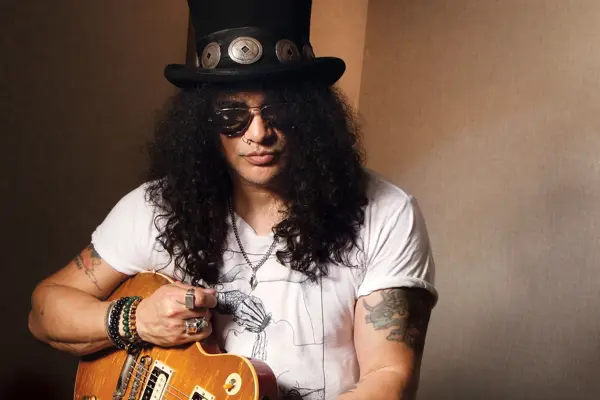 A man with long dark hair wearing a top hat and holding a guitar