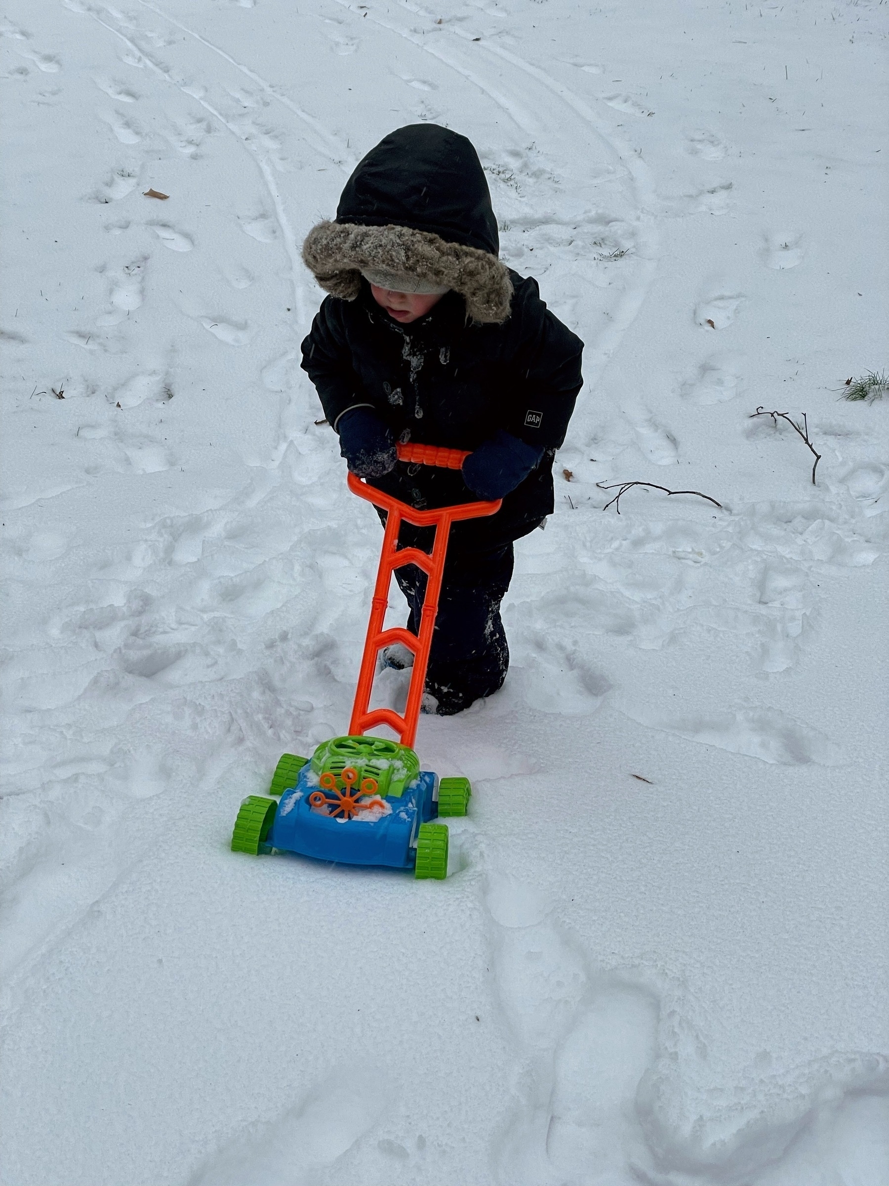 Child with a toy lawnmower in the snow