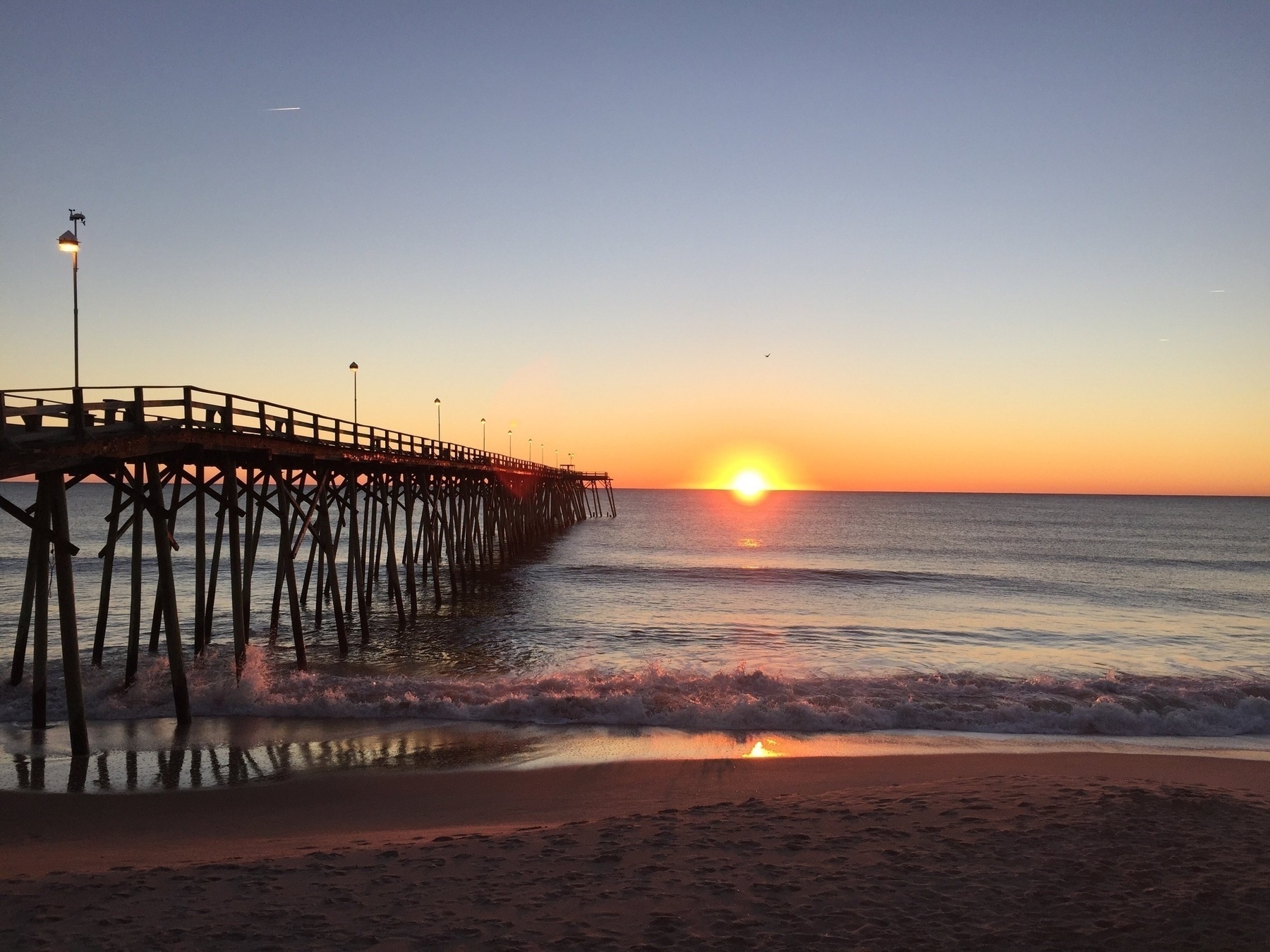 The photo shows a wooden pier extending into the ocean with the sun rising in the distance.