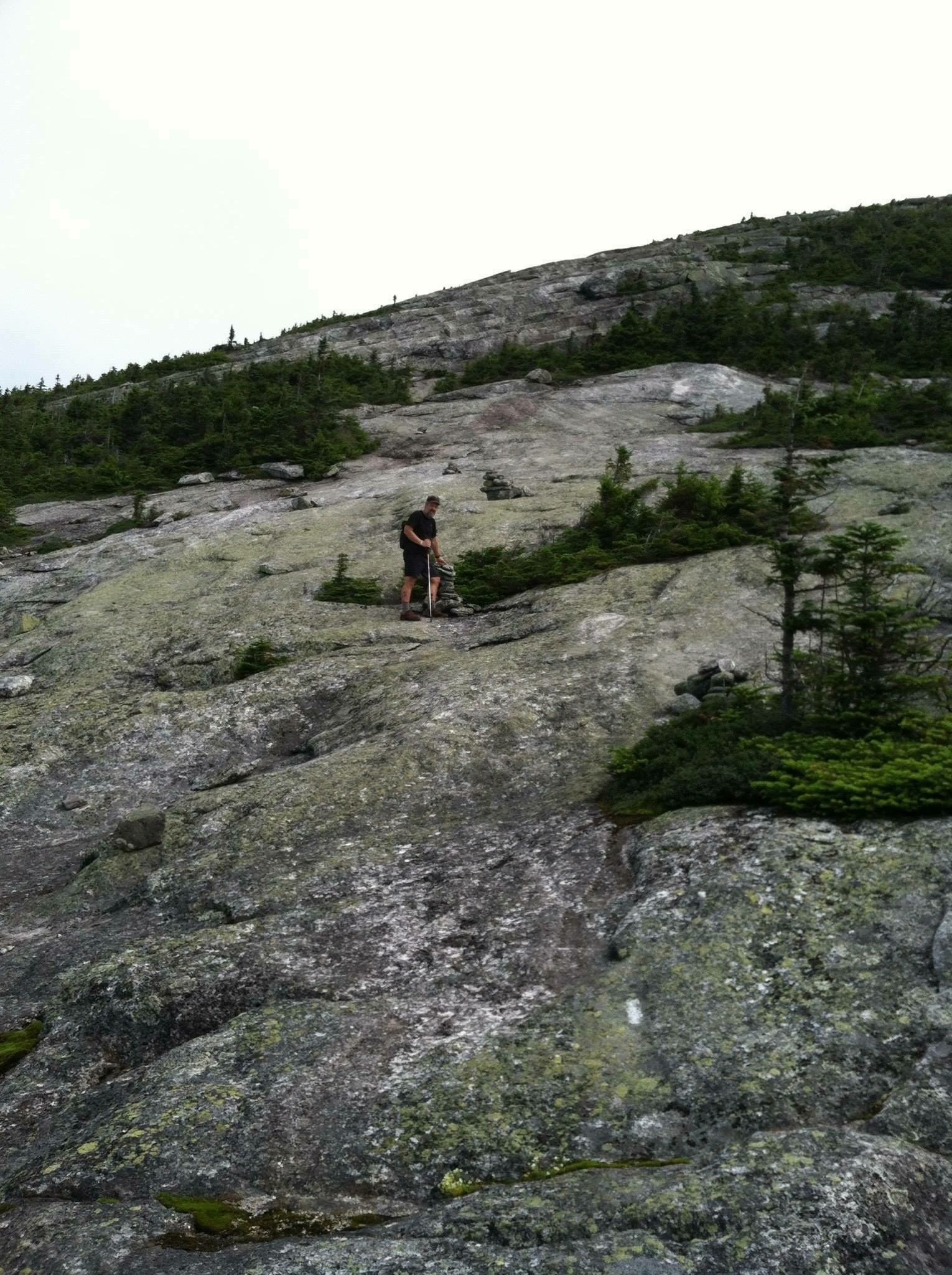 A hiker climbing an alpine bald mountain, a bare rockface