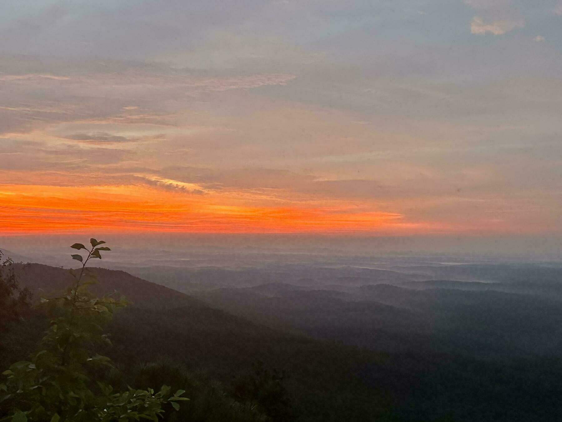 A vibrant sunset colors the sky in shades of orange and pink over a landscape of rolling hills.