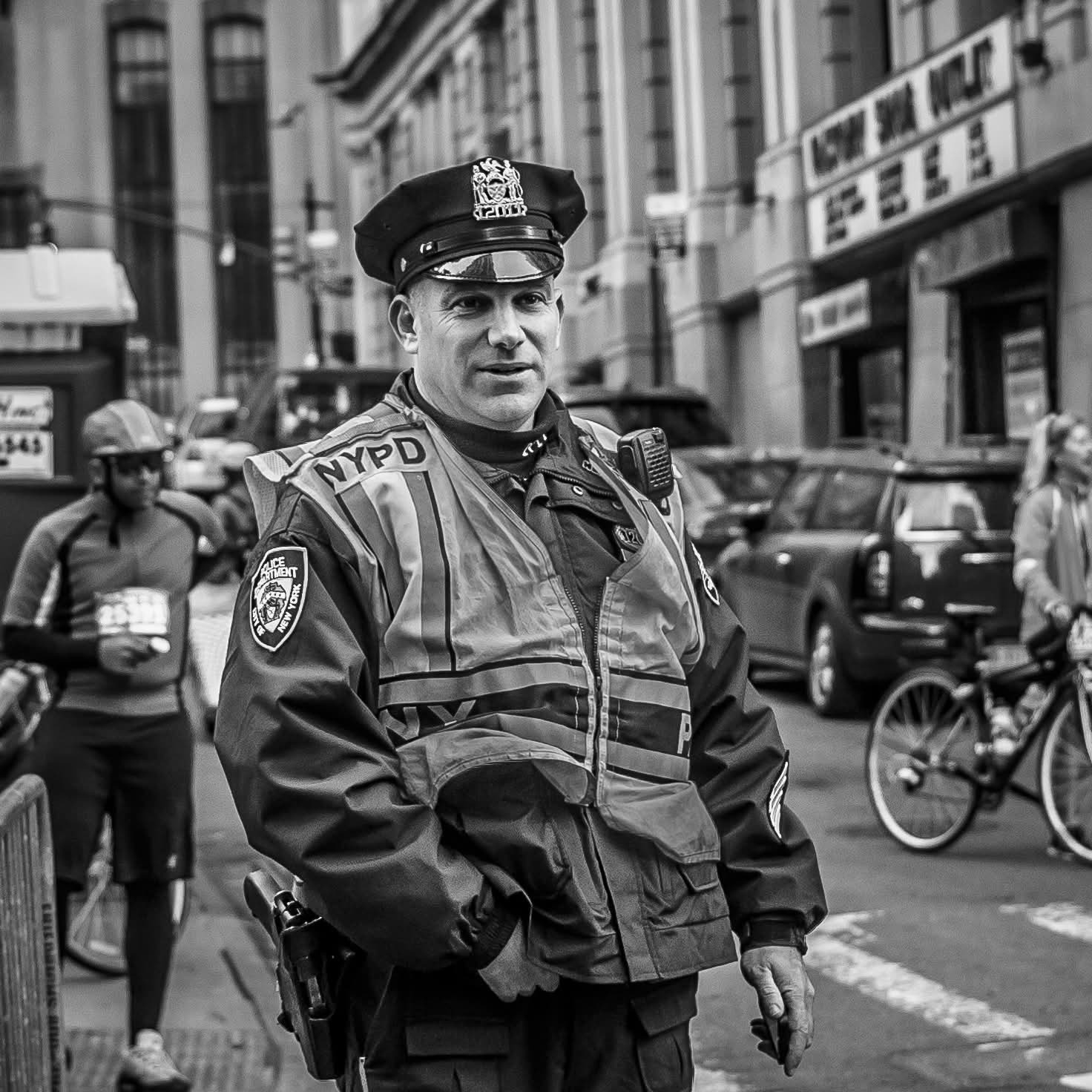 A police officer in uniform stands on a city street, surrounded by people and bicycles.