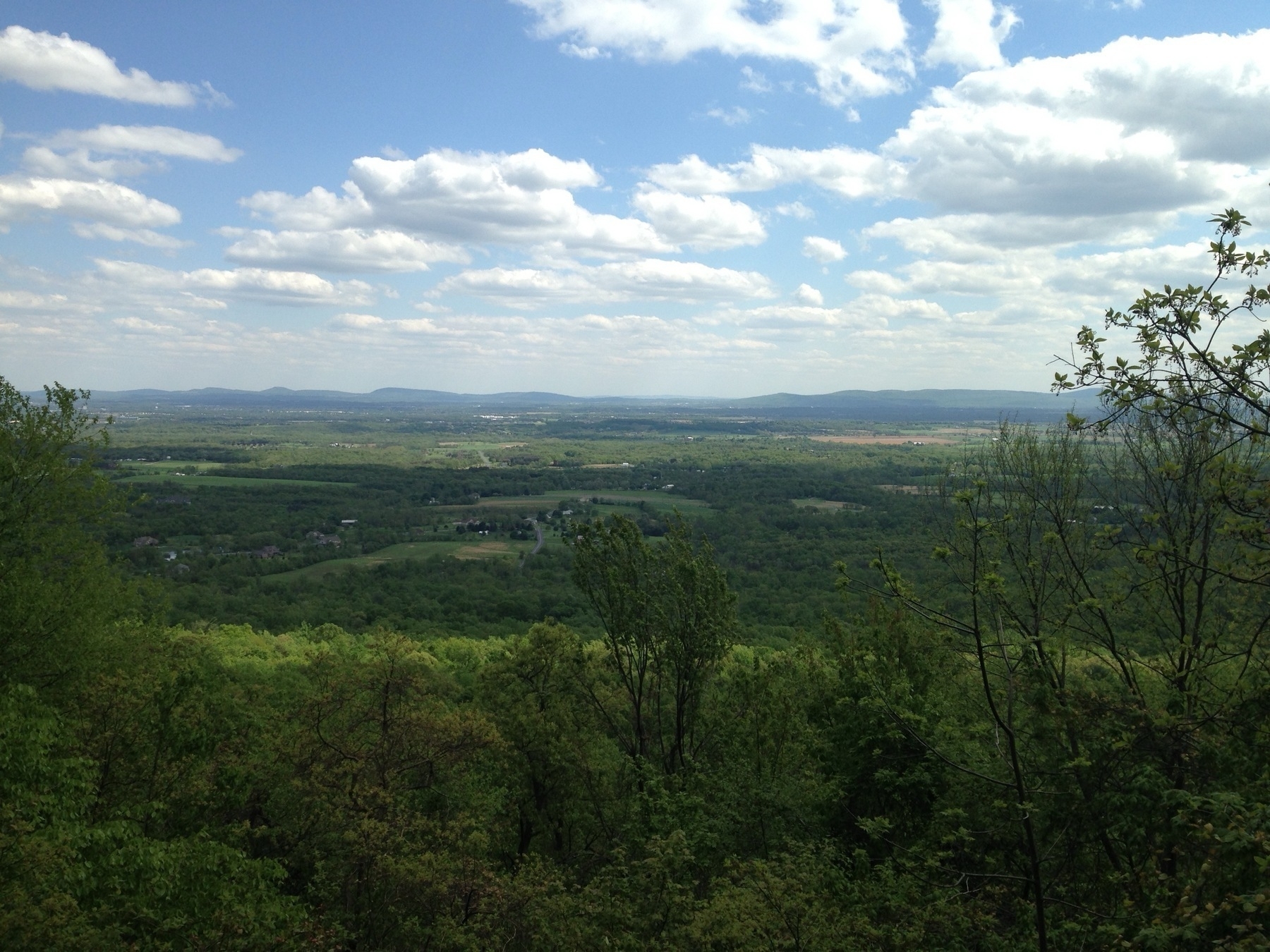 A scenic landscape features a lush green valley with hills in the distance under a partly cloudy sky.