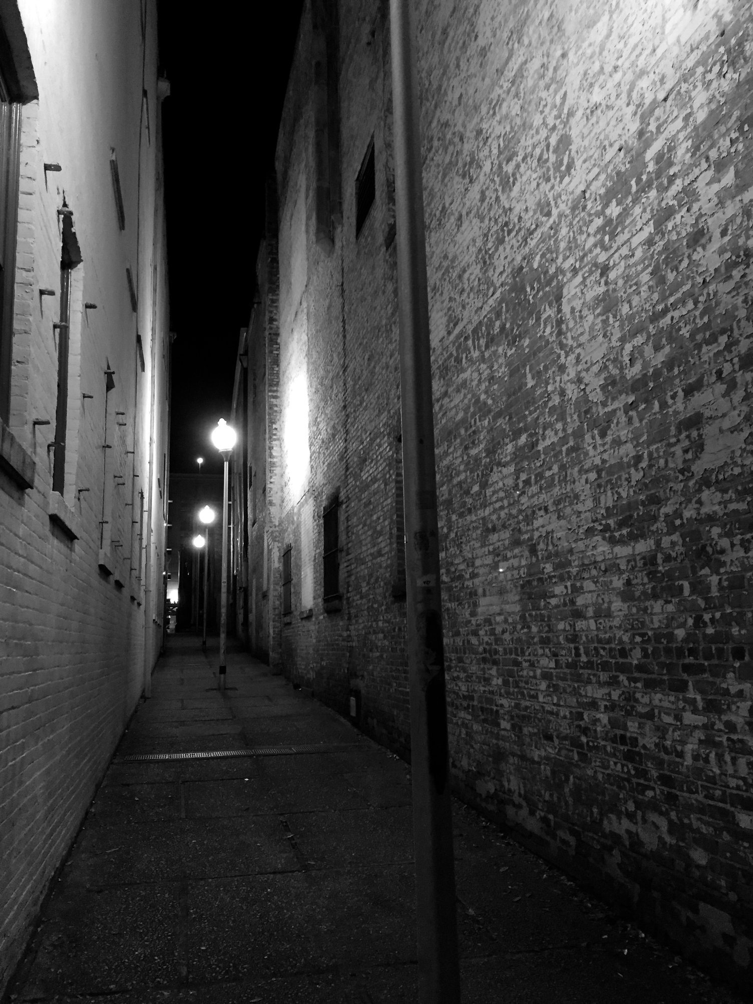 A narrow alleyway is illuminated by streetlamps at night, casting light on the textured brick walls.