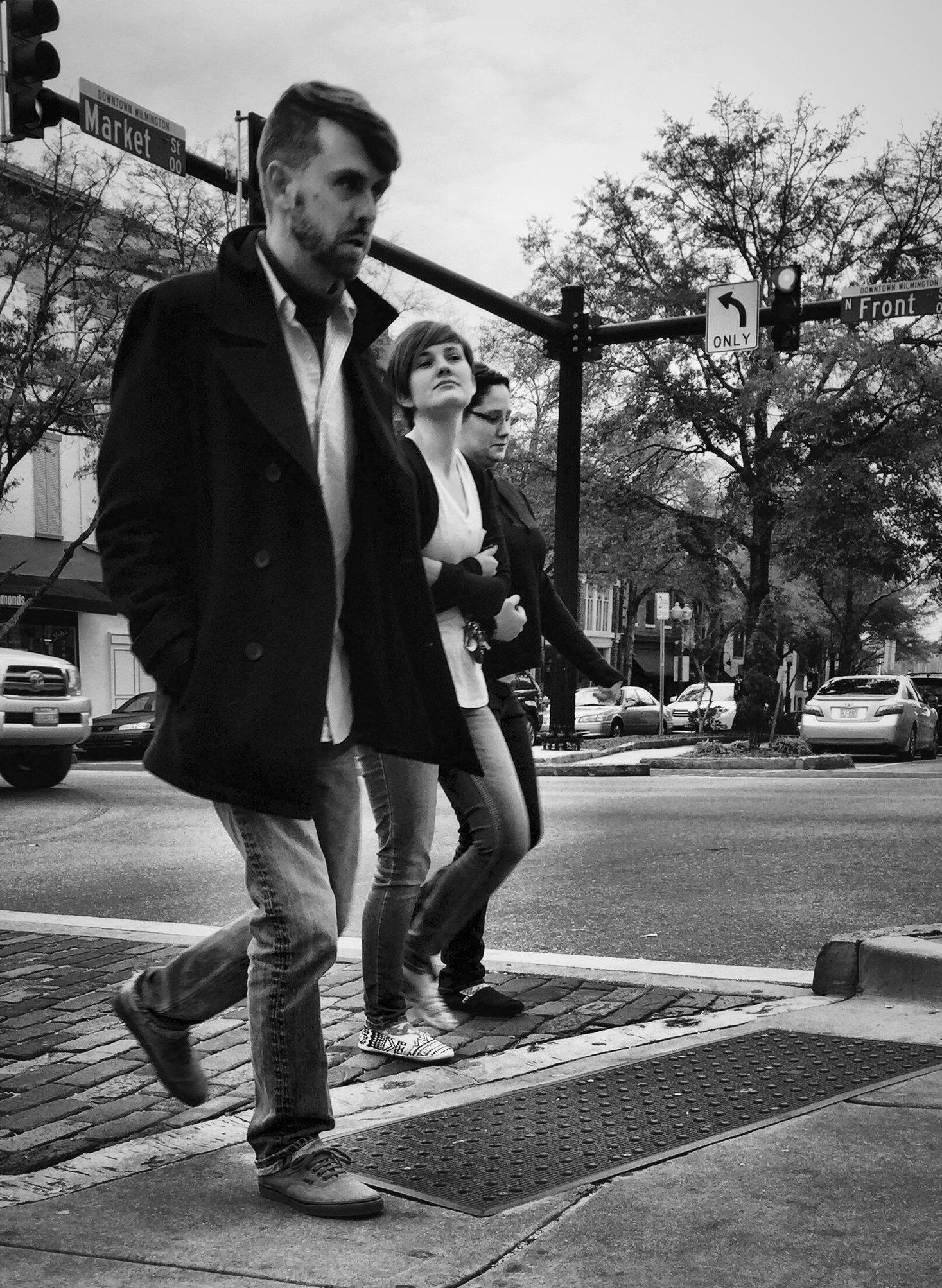 Three people are walking across a street in a city intersection on a cloudy day.