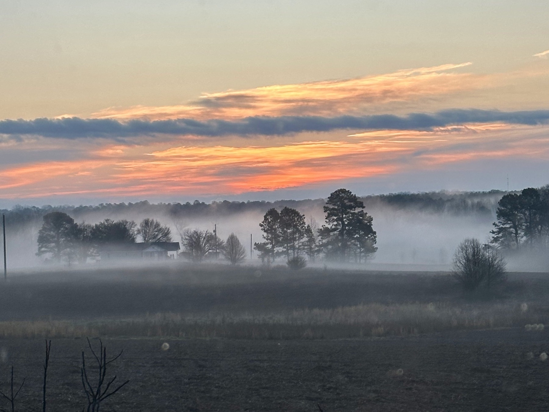 A foggy landscape features a rustic farm with trees silhouetted against a colorful sunrise.